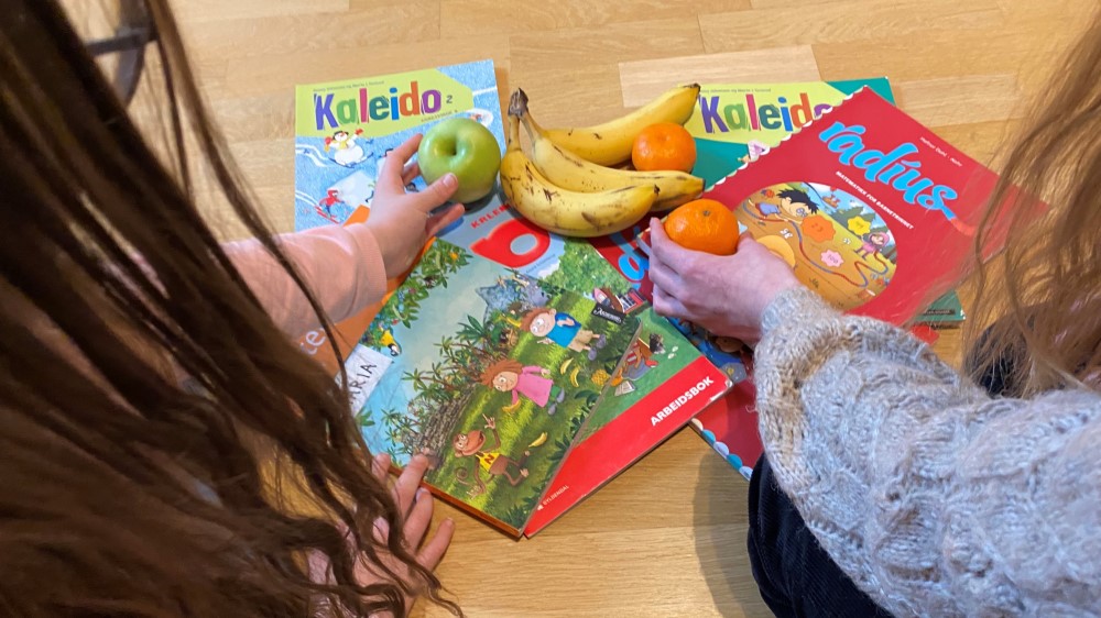 Image shows two children reaching out for fruits next to school books.