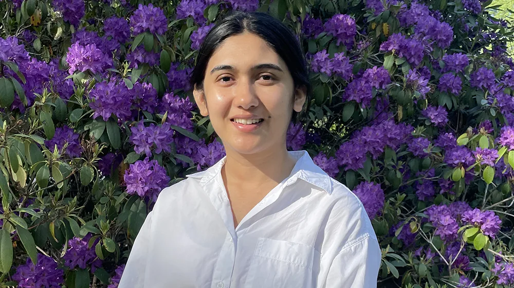 Young womn smiling in front of flowers.