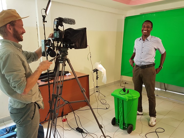 Man filming another man in front of a green screen background.