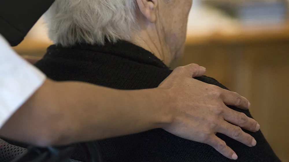 En sykepleier som legger hånden sin på skulderen til en eldre kvinne