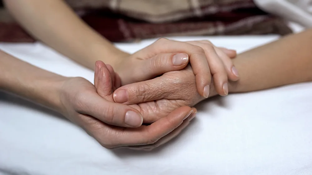 Two hands holding the hand of an elderly person
