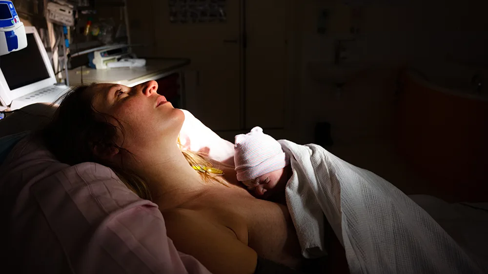 Kvinne som ligger i sykehusseng med spedbarn på brystet