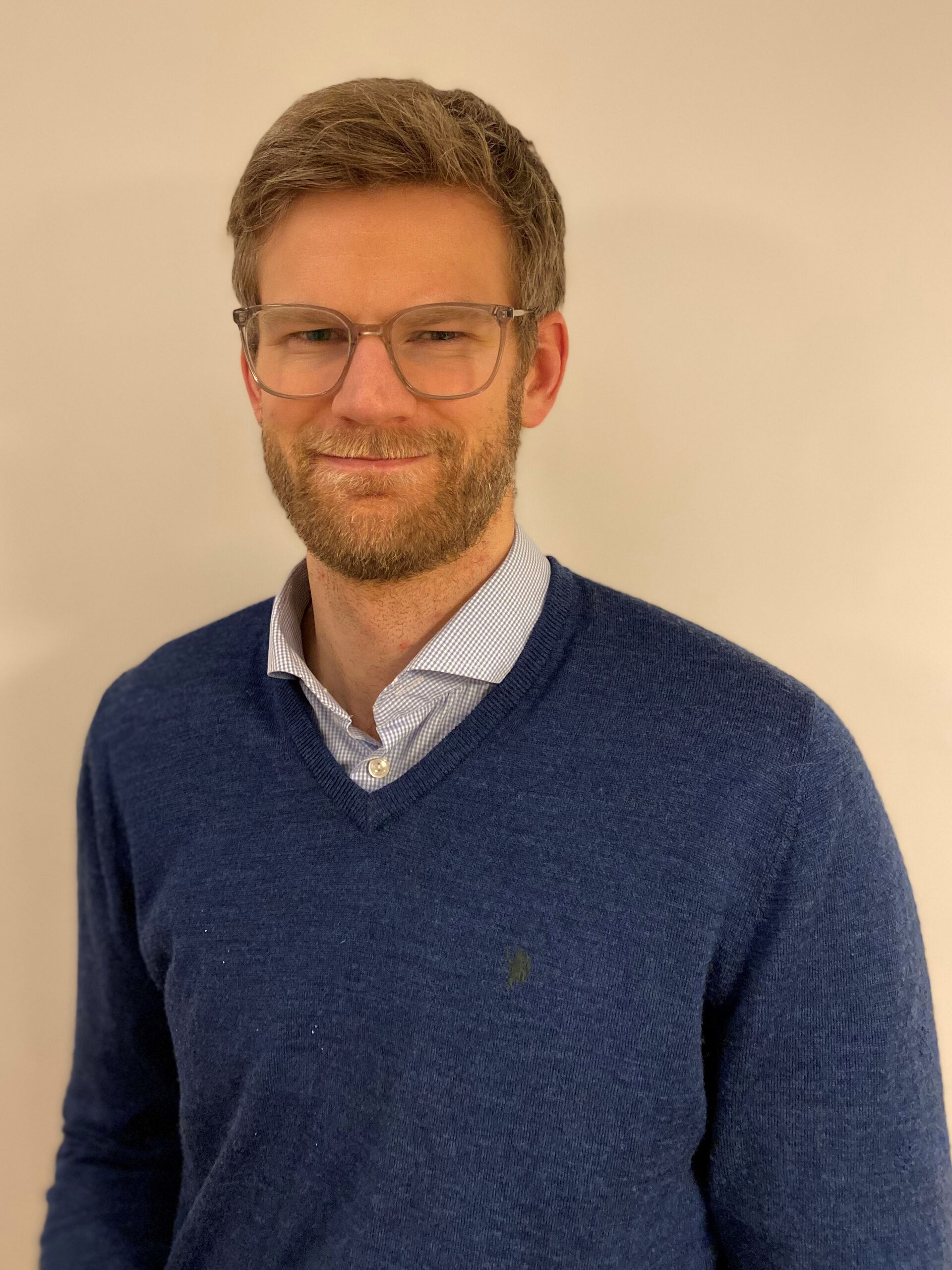 Mann, mellomblondt hår, briller, blå genser. Forsiktig smil.
