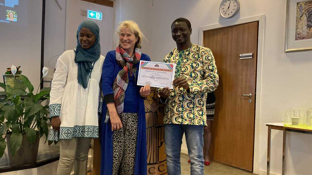Joanne Sundby står sammen med sine to gambiske studenter. Hun holder diplomet hun fikk fra den gambiske helseministeren.