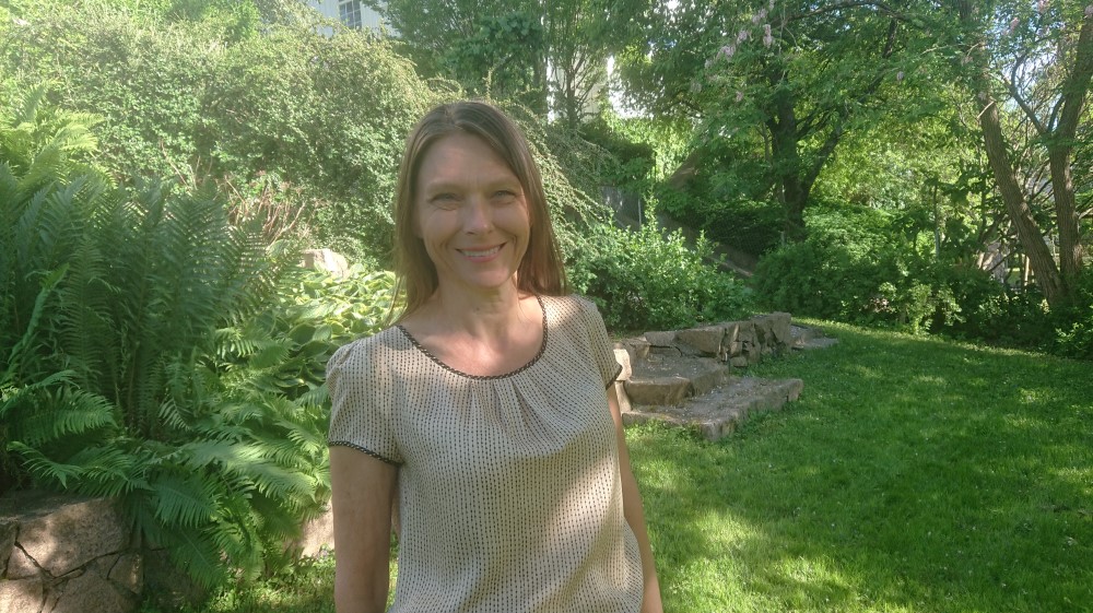 The picture shows a woman with brown hair in a garden