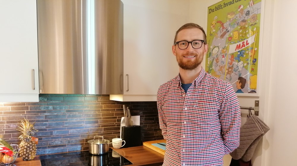 Bildet viser en mann med skjegg og briller som står på et kjøkken