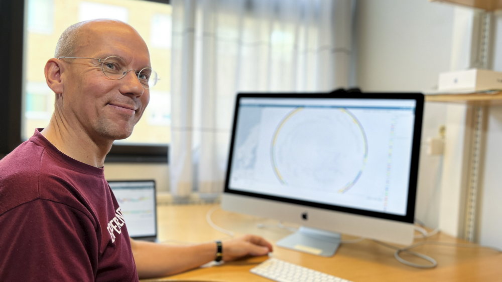 Jukka Corander sitter ved skrivebordet og smiler.