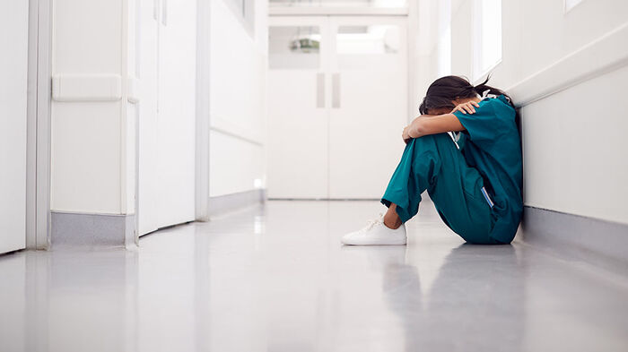 Ung kvinnelig kirurg sitter p? gulvet i en sykehuskorridor