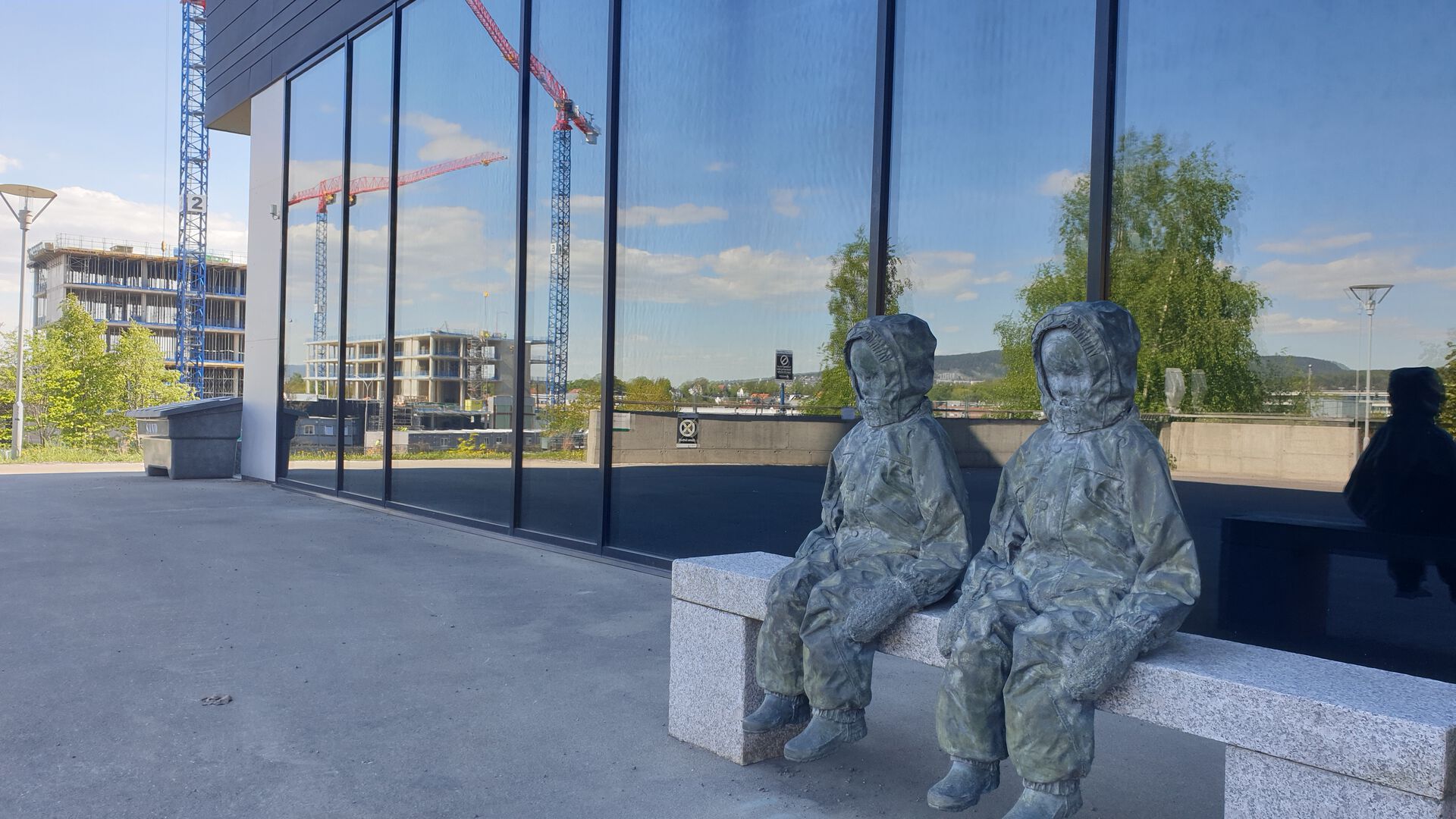 Heisekraner gjenspeiles i vinduene til Domus Medica, ved siden av statuene utenfor odontologi.
