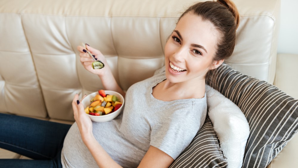 Bildet viser en gravid kvinne som spiser av en skål med fruktsalat