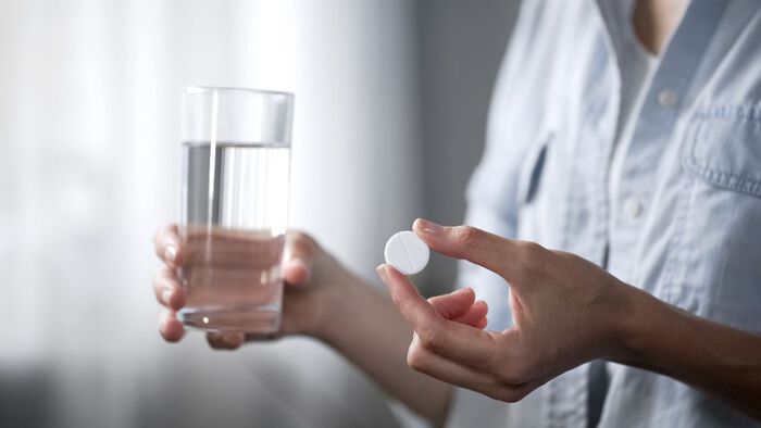 Bilde av en person som holder en pille og et vannglass.