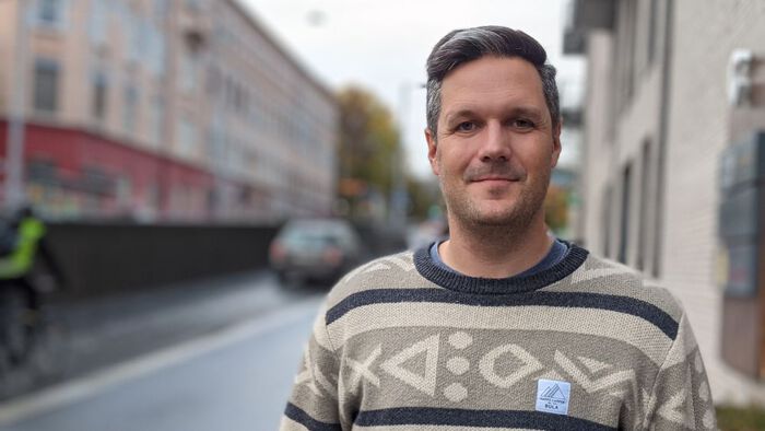 Ung mann med mørkt hår som står i gaten og smiler 