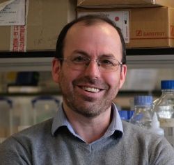 Headshot of David Kent, standing in a lab with carton boxes and glass bottles in the background