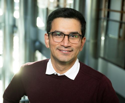 Profile picture of Rafa (dark hair and glasses), wearing a burgundy jumper with a white polo shirt. He is standing in a glass hallway.