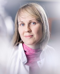 Dr. Emma Haapaniemi is wearing a pink roll neck jumper and a white lab coat. She has shoulder length blonde hair and is smiling.