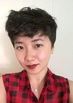 Ingrid Jin Schanke. She has short hair, wears red lipstick and is wearing a black and red checkered shirt. 