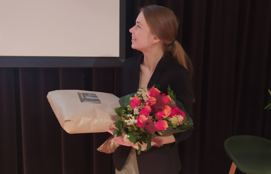Image of Karolina Spustova smiling and carrying a bouquet of pink flowers