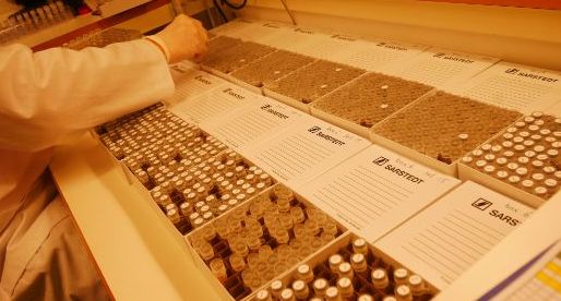 Bildet viser en person i et laoratorie som arbeider med flere esker som inneholder reagensrør med biologisk materiale