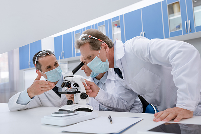 Tre forskere som ser i et mikroskop.