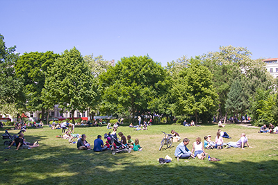 Solskinnsdag med gupper av mennesker på en plen i en park. 