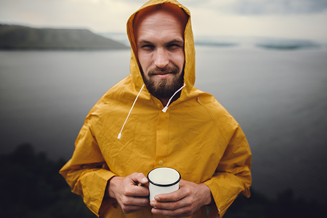 Mann i gul regnfrakk som holder en kaffekopp.