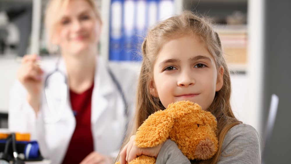 En jente som holder en teddybjørn og legen hennes.