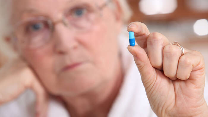 Eldre dame holder en pille mellom tommel og pekefinger