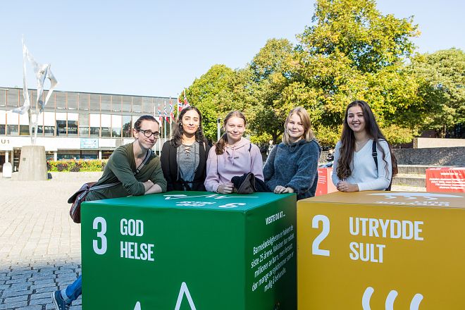 FNs bærekraftsmål 3 og 2, store bokser, og fem ungdommer