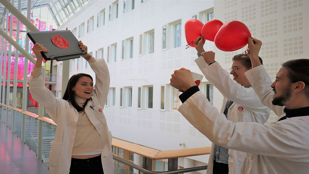 tre glade medisinstudenter som holder hjerteballonger