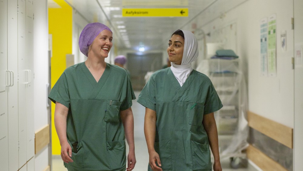 Bildet viser to studenter i sykehusuniform som går nedover en korridor