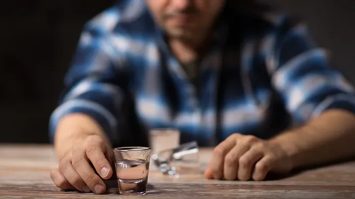 Mann som holder et glass i hånden, flere glass ligger veltet på bordet foran ham